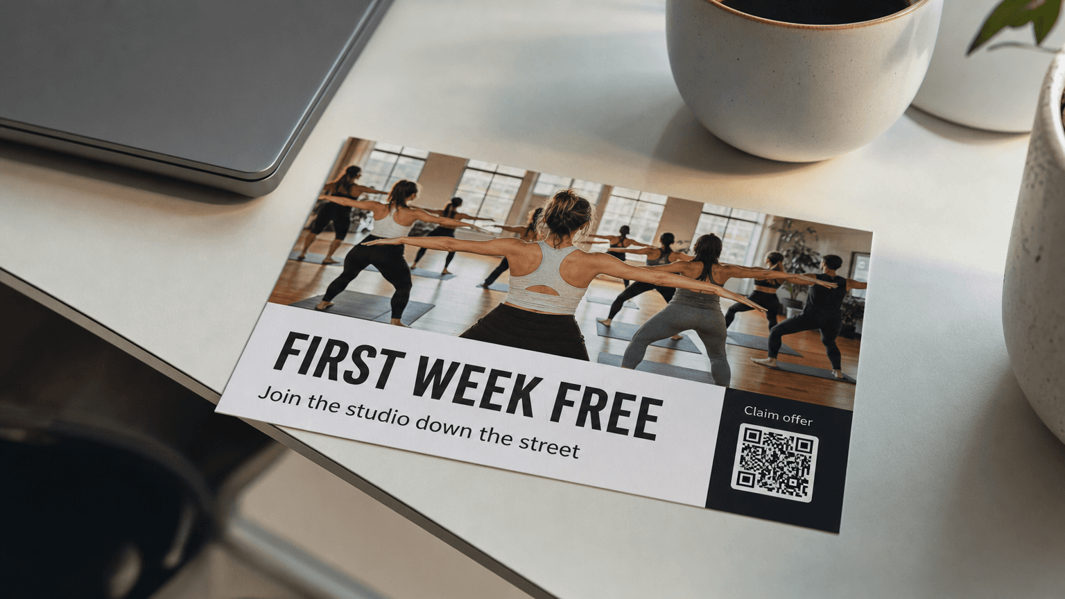 A gym postcard reading 'First Week Free' with a group fitness class photo, on a desk.